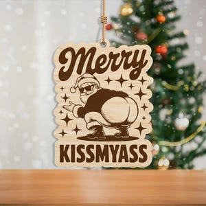 May include: Wooden Christmas ornament with a Santa Claus design. The ornament features the text "Merry" above an illustration of Santa squatting, with the text "Kiss My Ass" below. The ornament is hanging by a natural fiber string.