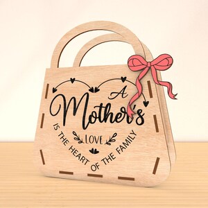 May include: A wooden gift bag with a pink bow and the text "A Mother's Love is the Heart of the Family".