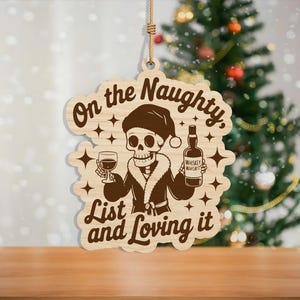 May include: Wooden Christmas ornament with a skeleton wearing a Santa hat and holding a glass of wine and a whiskey bottle. The text reads "On the Naughty List and Loving it". The ornament is hanging by a natural twine.