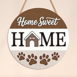 May include: A round wooden sign with the words "Home Sweet HOME" in white and black. The sign features a dog house graphic and paw prints, with a brown and white color scheme, and a rope for hanging.