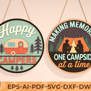 May include: Two round wooden signs with camping themes. One says "Happy Campers" with a camper illustration. The other says "Making Memories One Campside at a Time" with a tent and two figures. Both signs are hanging by twine.