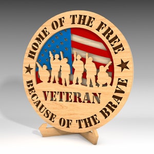 May include: Wooden round sign with the text "HOME OF THE FREE BECAUSE OF THE BRAVE VETERAN". The sign features a silhouette of soldiers in front of an American flag design. The sign is displayed on a wooden stand.