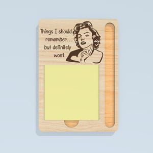 May include: Wooden memo pad with a portrait of a woman and the text "Things I should remember... but definitely won't." The pad has a slot for a pen and a yellow sticky note pad.