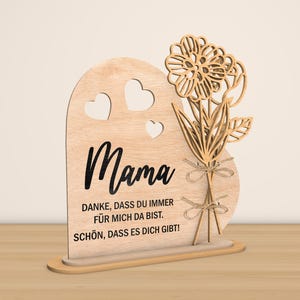 May include: Wooden heart-shaped sign with a cutout flower design and the text "Mama" in black. The sign also includes the text "Danke, dass du immer f&uuml;r mich da bist. Sch&ouml;n, dass es dich gibt!"