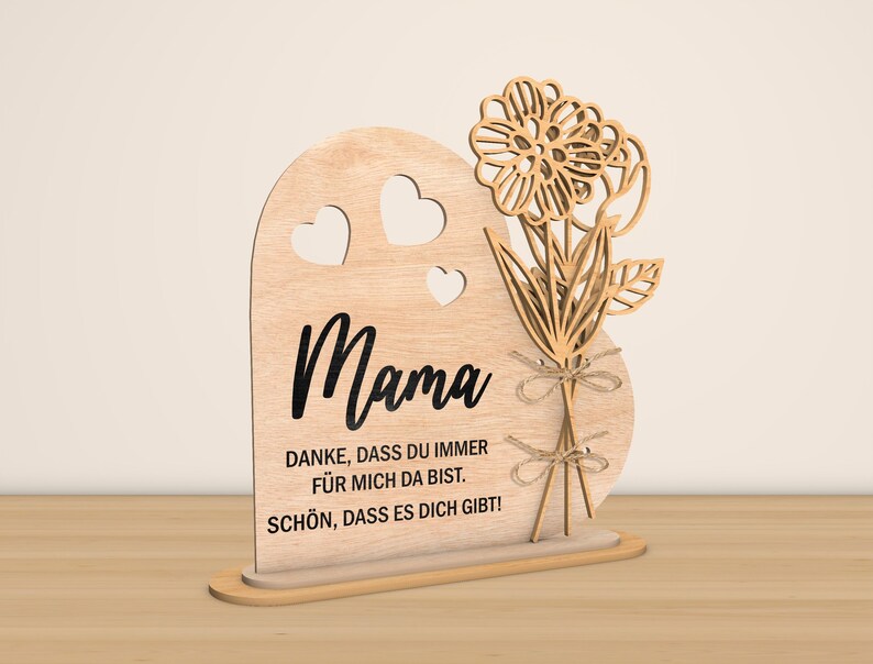 May include: Wooden heart-shaped sign with a cutout flower design and the text "Mama" in black. The sign also includes the text "Danke, dass du immer f&uuml;r mich da bist. Sch&ouml;n, dass es dich gibt!"