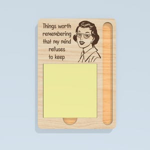 May include: Wooden memo board with a retro illustration of a woman wearing glasses. The board has a slot for a notepad and the text "Things worth remembering that my mind refuses to keep."