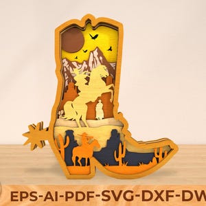 May include: A wooden cutout of a cowboy boot with a western scene inside. The boot is brown and the scene includes a sunset, mountains, and cowboys on horseback.