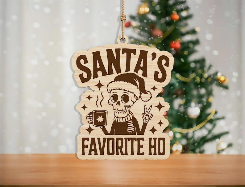 May include: Wooden Christmas ornament with the text "SANTA'S FAVORITE HO". The ornament features a skeleton wearing a Santa hat and scarf, holding a mug and giving a peace sign. The ornament is hanging by a rope.