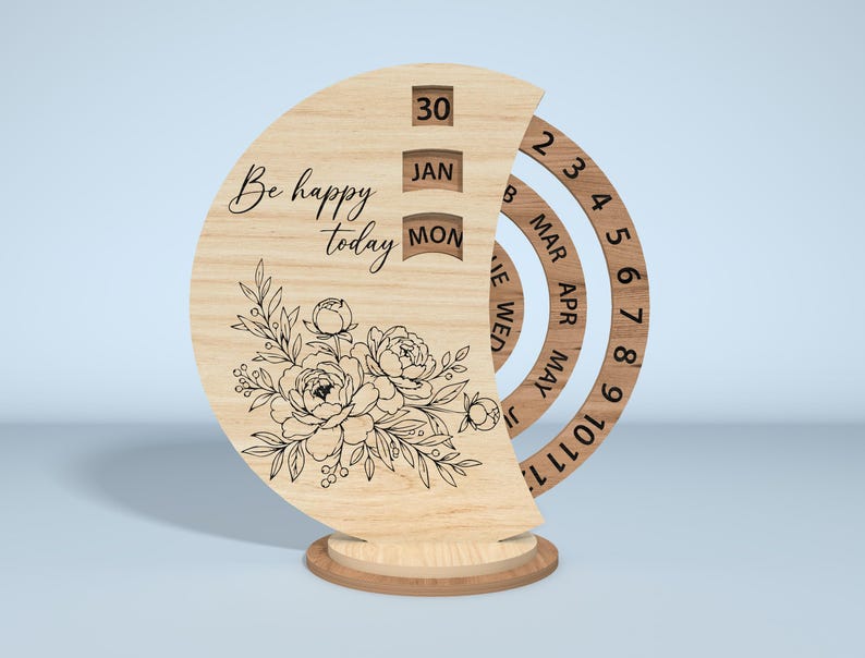 Puede incluir: Calendario perpetuo de madera con dise&ntilde;o floral y la frase "Be happy today". El calendario muestra la fecha, el mes y el d&iacute;a. Tiene una base redonda y anillos giratorios para el mes y el d&iacute;a.
