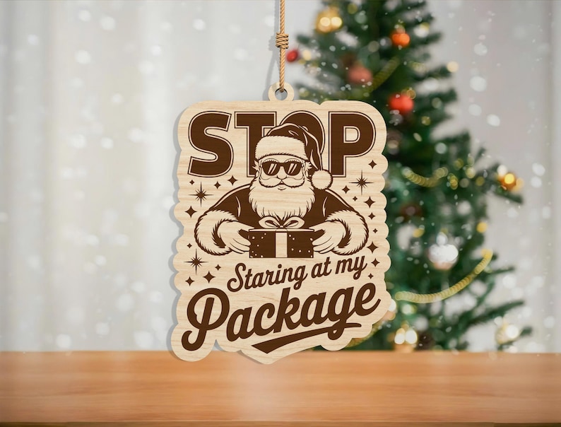 May include: Wooden Christmas ornament featuring a Santa Claus graphic wearing sunglasses and holding a gift. The ornament has the text "STOP Staring at my Package" in a playful font. The ornament hangs from a natural twine.
