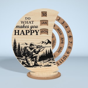 Puede incluir: Calendario perpetuo de madera con una ilustraci&oacute;n de cazador y el texto "Do what makes you HAPPY". El calendario presenta anillos giratorios para el mes y el d&iacute;a, con una base para sostenerlo. El cazador est&aacute; arrodillado y apuntando con un rifle.