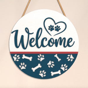 May include: A round wooden sign with the word "Welcome" in navy blue script. The top half is white, with a heart and paw prints. The bottom half is navy blue with paw prints and bone shapes. A red stripe separates the two halves.