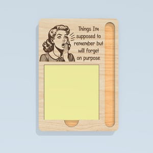 May include: Wooden memo board with a retro illustration of a woman and the text "Things I'm supposed to remember but will forget on purpose." Includes a yellow sticky note pad and a pen holder.