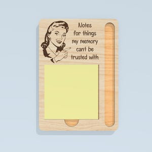 May include: Wooden memo board with a retro illustration of a woman pointing, and the text "Notes for things my memory can't be trusted with." Includes a yellow sticky note pad and a slot for a pen or pencil.