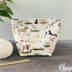 May include: A fabric storage pouch featuring a cream-colored background with a repeating pattern of watercolor-style farm animals, including horses, cows, pigs, chickens, and dogs, with two small wooden buttons at the top center opening.