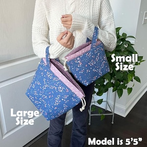 A person is holding two bags, one large and one small, with a plant in the background.