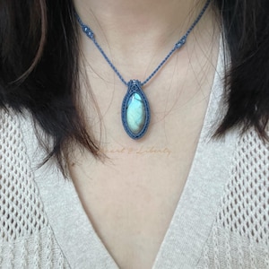 Può includere: Una collana in macramè blu fatta a mano con un ciondolo a forma di goccia con una pietra iridescente scintillante. La collana è indossata intorno al collo, mettendo in mostra gli intricati nodi e le sottili variazioni di colore della pietra. Il ciondolo è lungo circa 3,8 cm.