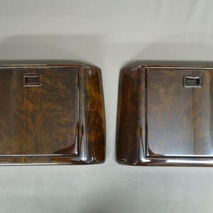 May include: Two matching rectangular wooden panels with a glossy finish and a dark brown wood grain pattern. Each panel has a chrome-colored border and a small rectangular handle. The panels appear to be part of a larger item.