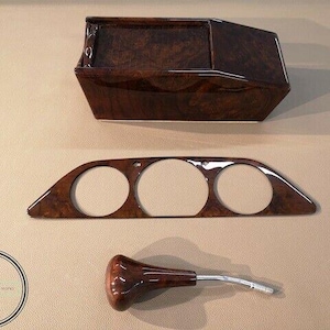May include: A set of car interior wood trim pieces. The set includes a rectangular console, a panel with three circular openings, and a gear shift knob. All pieces have a glossy, dark brown wood grain finish.
