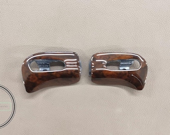 May include: Two matching car interior trim pieces. The trim is a dark brown wood grain with a glossy finish. Each piece has a silver metal bracket and a white accent line.
