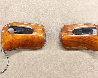 May include: Two wooden car interior trim pieces with a glossy finish. The trim has a natural wood grain pattern in shades of brown and amber. Each piece has a dark opening and a pinkish-purple accent.