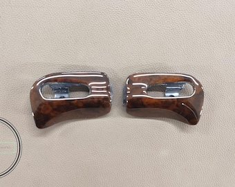 May include: Two matching car interior trim pieces. The trim is a dark brown wood grain with a glossy finish and a silver accent. The pieces are curved and have a rectangular opening.