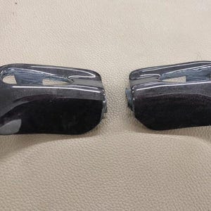 May include: Two glossy black automotive door handles. The handles have a curved design with a recessed area for gripping. The image is taken from a slightly elevated angle, showing the top and side of the handles.