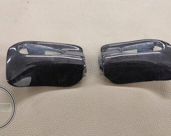 May include: Two glossy black automotive door handles. The handles have a curved design with a recessed area for gripping. The image is taken from a slightly elevated angle, showing the top and side of the handles.