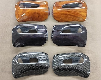 May include: Eight car key fob covers in various styles. The top row features a dark wood grain finish, the second row has a lighter wood grain, the third row is a dark metallic, and the bottom row is carbon fiber.