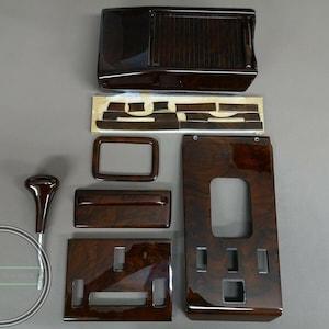 May include: A collection of dark wood-grain interior car trim pieces. The set includes a console, various panels, a gear shift knob, and other components. The pieces have a glossy finish and are arranged on a neutral background.