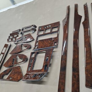 Könnte beinhalten: Eine Sammlung glänzender Zierteile für den Innenraum eines Fahrzeugs in Holzoptik. Das Set umfasst verschiedene Formen und Größen, wie lange Streifen, rechteckige Paneele und konturierte Teile, alle mit einer satten, dunkelbraunen Oberfläche und sichtbarer Holzmaserung.