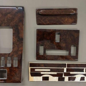 May include: A set of five dark brown woodgrain interior trim pieces. The largest piece has a rectangular cutout and several smaller openings. The other pieces include a rectangular panel with a handle, a panel with two openings, and a strip of smaller pieces.