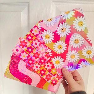 May include: Three sheets of holographic paper with pink, red, yellow, and white daisy patterns. The paper has a glittery finish.