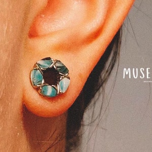 Puede incluir: Primer plano de un pendiente circular azul y blanco con un centro negro. El pendiente está hecho de varias piezas de turquesa y piedra blanca.