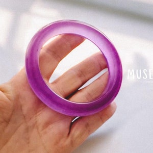 May include: A purple bangle bracelet made of smooth, translucent material. The bracelet is round and has a glossy finish.