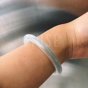 May include: A light grey jade bangle bracelet on a person's wrist.