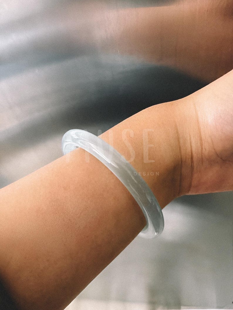 K&ouml;nnte beinhalten: Ein hellgraues Jade-Armband an einem Handgelenk.