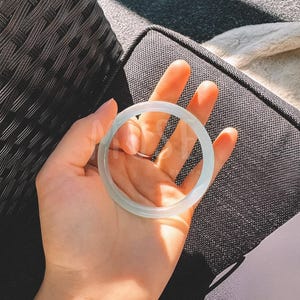 K&ouml;nnte beinhalten: Ein wei&szlig;es Jade-Armband. Das Armband ist glatt und poliert und hat eine zarte, durchscheinende Qualit&auml;t.