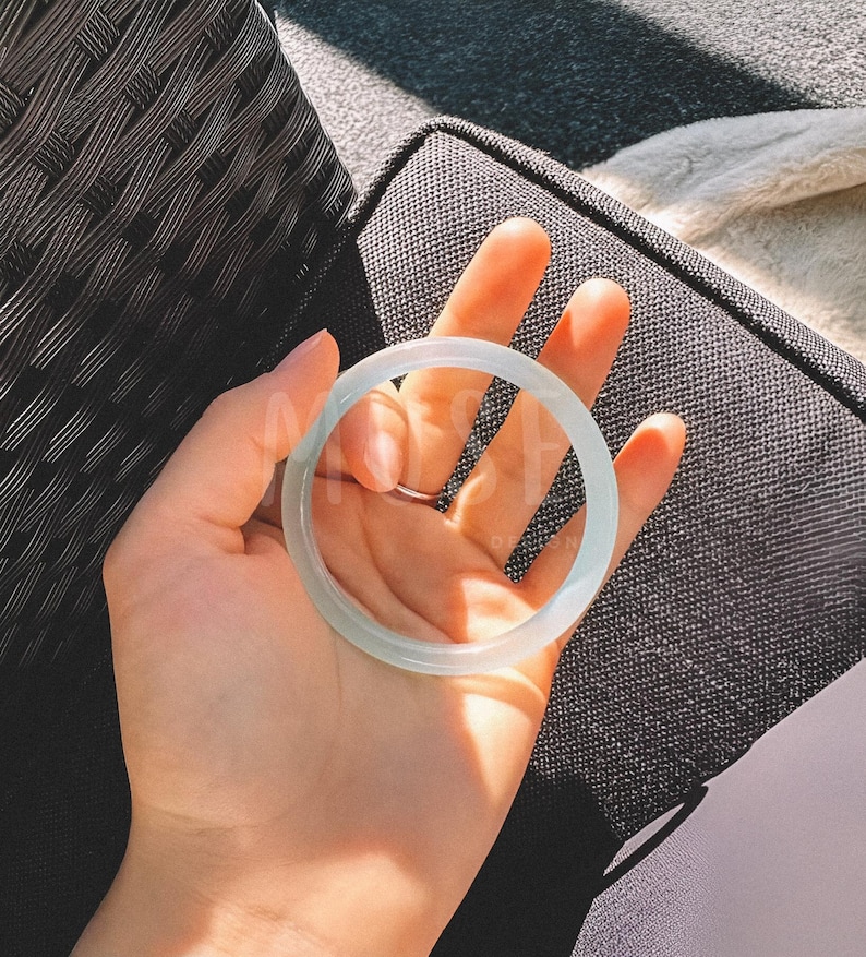 K&ouml;nnte beinhalten: Ein wei&szlig;es Jade-Armband. Das Armband ist glatt und poliert und hat eine zarte, durchscheinende Qualit&auml;t.