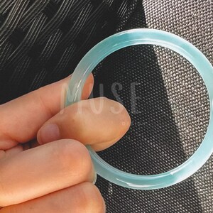 K&ouml;nnte beinhalten: Ein hellblaues Jade-Armband. Das Armband ist glatt und poliert.