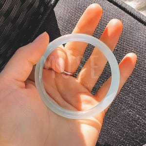 K&ouml;nnte beinhalten: Ein wei&szlig;es Jade-Armband. Das Armband ist glatt und poliert und hat eine leicht durchscheinende Optik.