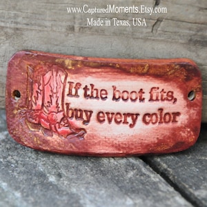 May include: A red leather tag with gold accents and a red cowboy boot design. The tag has the text "If the boot fits, buy every color" embossed on it.