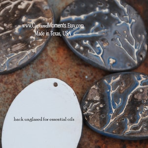 May include: Four ceramic oval-shaped ornaments with a white tree branch design on a dark blue and brown background. The back of one ornament is white and unglazed, with the text "back unglazed for essential oils". The text "www.CapturedMoments.Etsy.com Made in Texas, USA" is visible on the image.