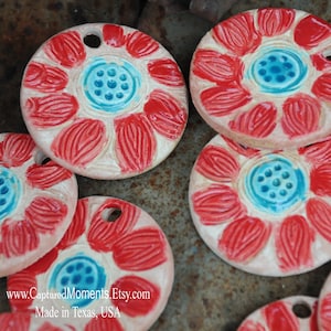 May include: A set of six ceramic ornaments featuring a red flower design with a blue center. The ornaments are round and have a hole at the top for hanging. The ornaments are made in Texas, USA.