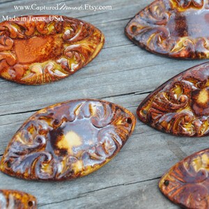 May include: Six ceramic oval-shaped embellishments with intricate floral designs. The embellishments are glazed in shades of brown, yellow, and white.