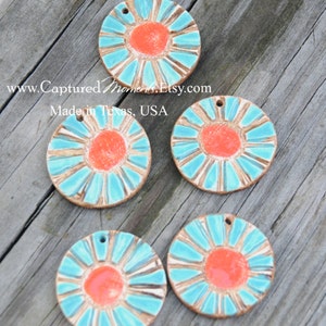 May include: Five ceramic round ornaments with a turquoise blue and orange sunburst design. The ornaments have a hole at the top for hanging.