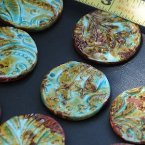 May include: A collection of round, ceramic tiles with a turquoise glaze and brown accents. The tiles feature intricate floral and leaf patterns.
