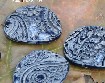 May include: Four blue ceramic oval-shaped pendants with a white paisley design. The pendants have a textured surface and are made in Texas, USA.