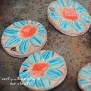 May include: Four ceramic ornaments with a blue and orange floral design. Each ornament features a stylized flower with a light blue center and orange petals. The ornaments are made in Texas, USA.
