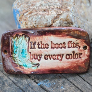 May include: A brown ceramic tile with a white background and a blue and green boot design. The tile has the text "If the boot fits, buy every color" on it.